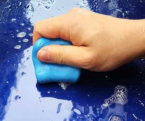 A hand rubbing a piece of Professional cleaning clay over a wet, soapy car panel.