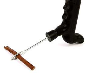 Close-up of theTire Repair Kit featuring a black T-handle insertion tool with a brown rubber plug strip threaded through its needle eye, ready for tire repair.