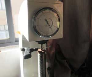 Close-up of a hardness testing machine checking the durability of the black plastic T-handle tool grip. The dial gauge confirms the pass result.